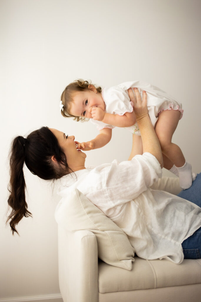 mom holding giggling toddler daughter above head 