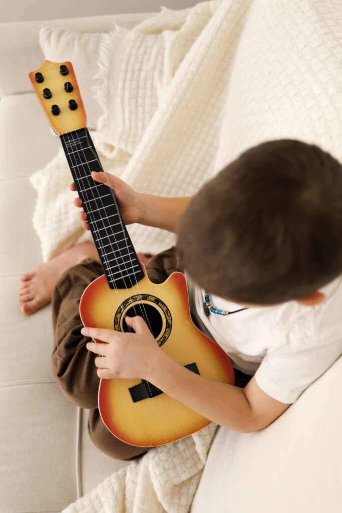 boy playing mini guitar cozy on couch