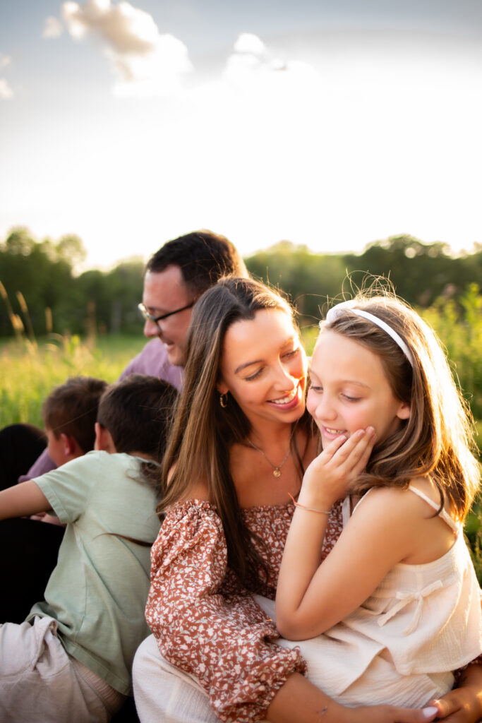 mother affectionately looking at daughter during long island family photo session with husband and sons in background