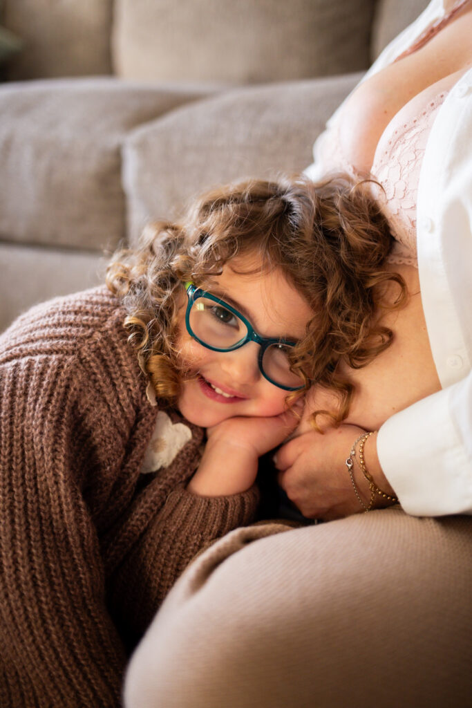 toddler girl leaning on pregnant mother's belly during in-home maternity photo session