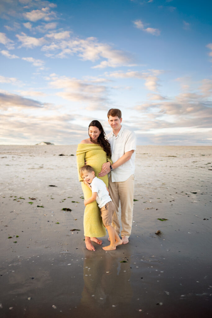 expecting mother husband and son embracing during point lookout maternity beach photo session 