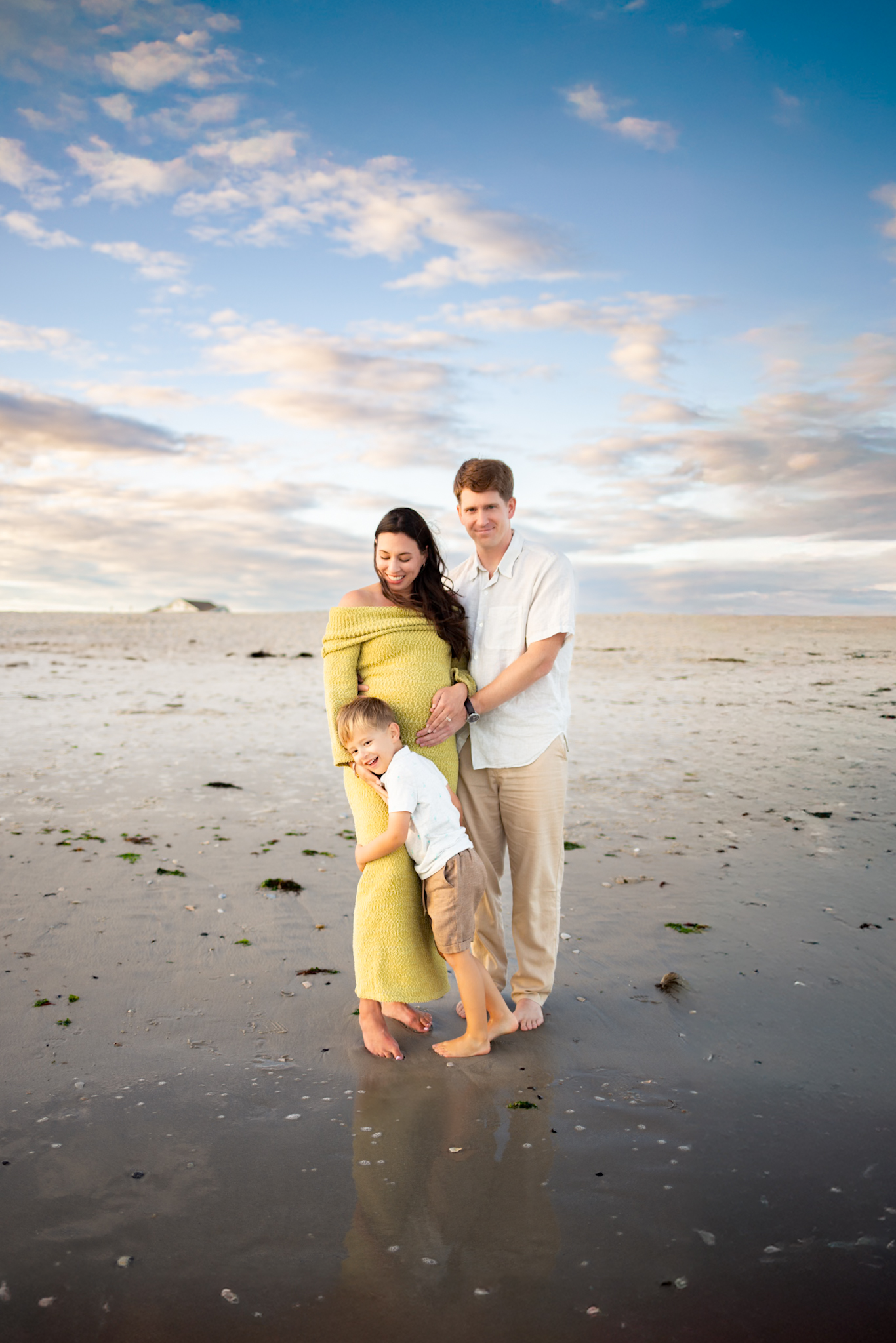 mother father and son on beach at golden hour embracing during maternity family photo session