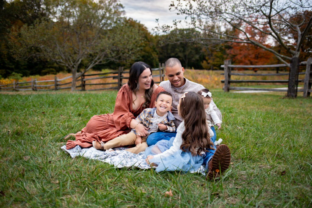 family sitting on blanket in orchard giggling 